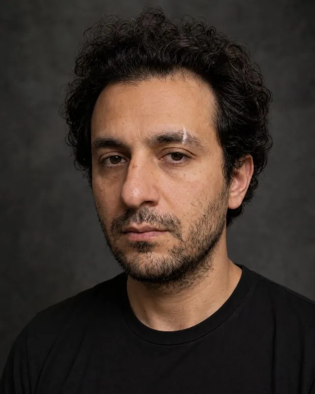 Actor: a theatrical headshot against a mottled dark grey backdrop, plain black t-shirt
