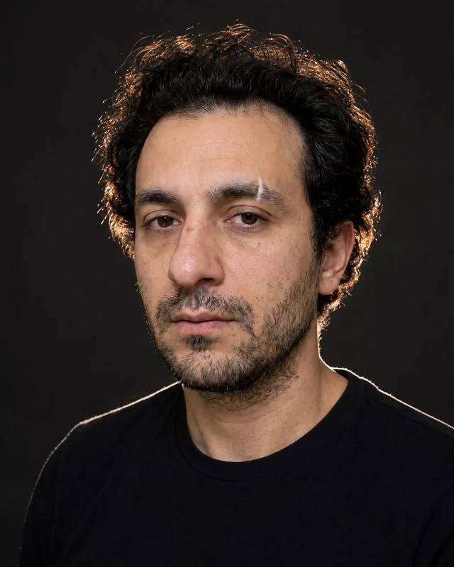 Actor: a close crop with a bright rim light behind the shoulder, plain black t-shirt, dark background