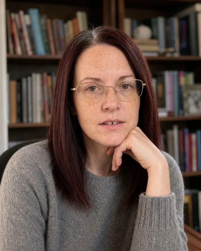 Author: seated in a book-lined study with soft window light from the left, wearing a wool jumper