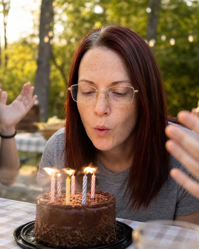 Birthday picnic: blowing out candles with friends’ hands clapping out of focus, warm afternoon glow