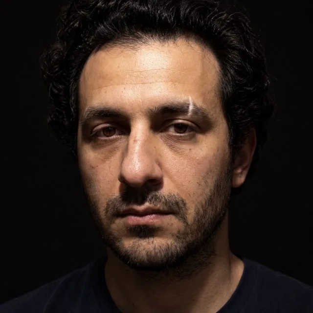 Extreme close-up: a close crop lit by a single hard light from above, deep shadows under the brow, direct gaze