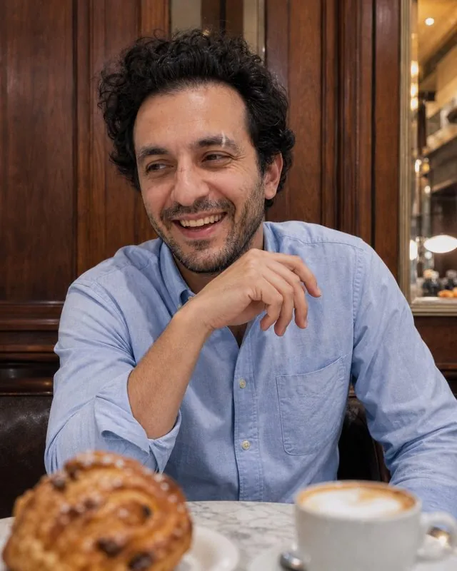 Coffee shop: at a small marble table mid-laugh, blue oxford shirt with the sleeves rolled