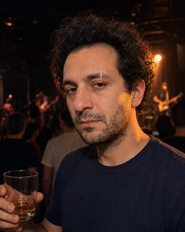 Live music: in a small dim music venue with a drink in hand, warm stage light spilling across the face