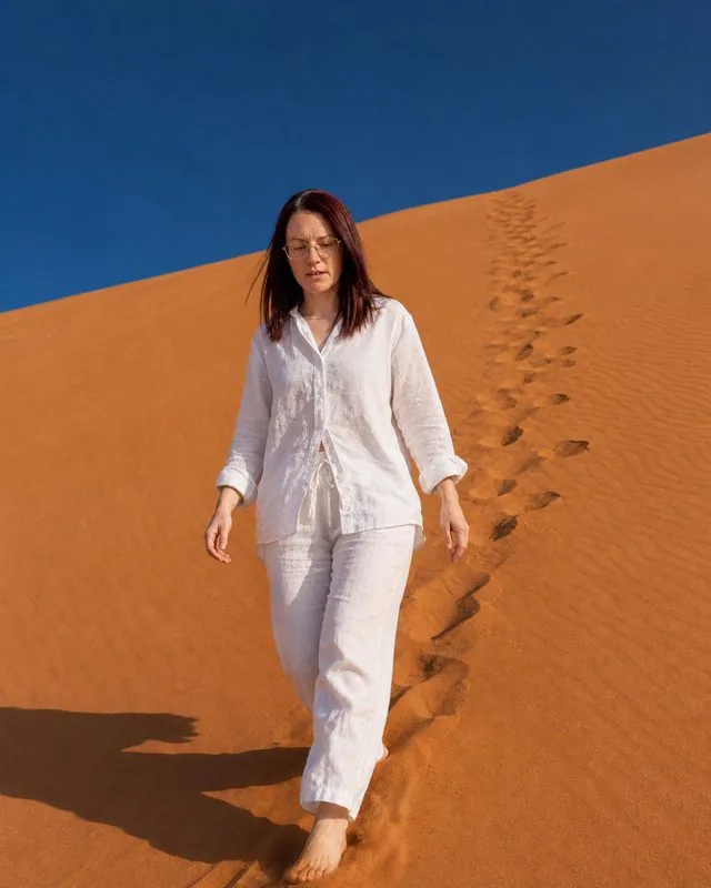 Desert dunes: walking down a dune face in loose white linen, footprints trailing behind, deep orange sand and cobalt sky
