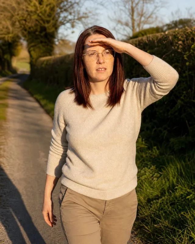 Engagement shoot: walking a country lane hand raised to shade the eyes, soft knit and cotton trousers