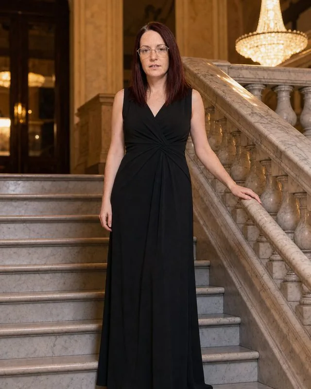Evening wear: in a floor-length black evening gown on a marble staircase, warm chandelier light, one hand on the banister