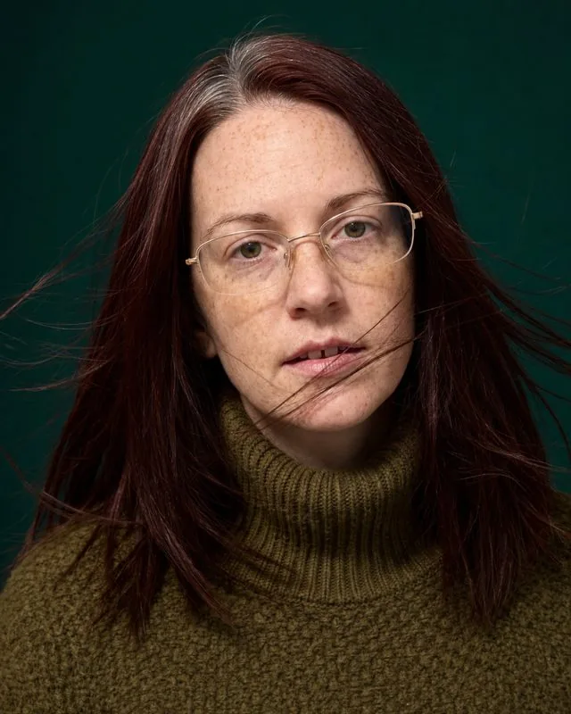 Editorial: a close editorial crop with a wind machine lifting the hair, high-necked knit, saturated backdrop