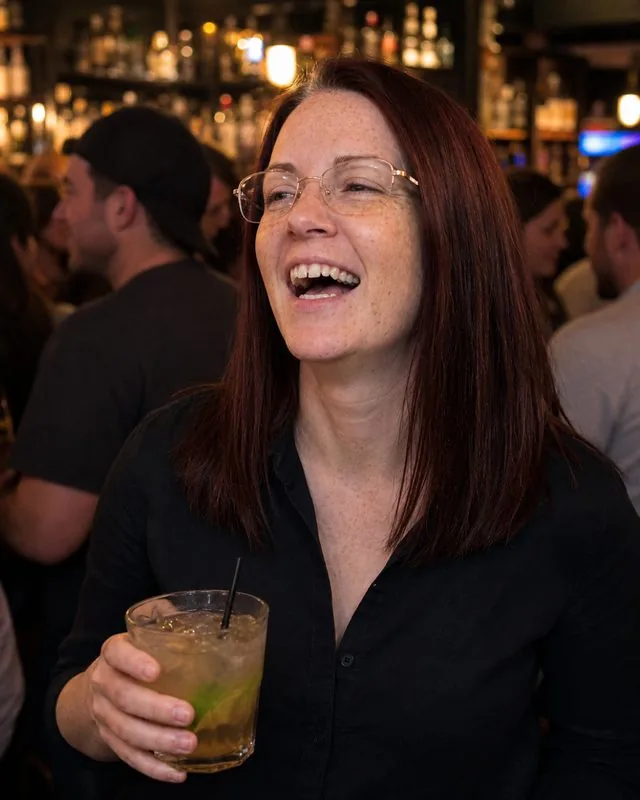Night out: in a busy bar holding a drink, dark shirt open at the collar, warm amber lighting