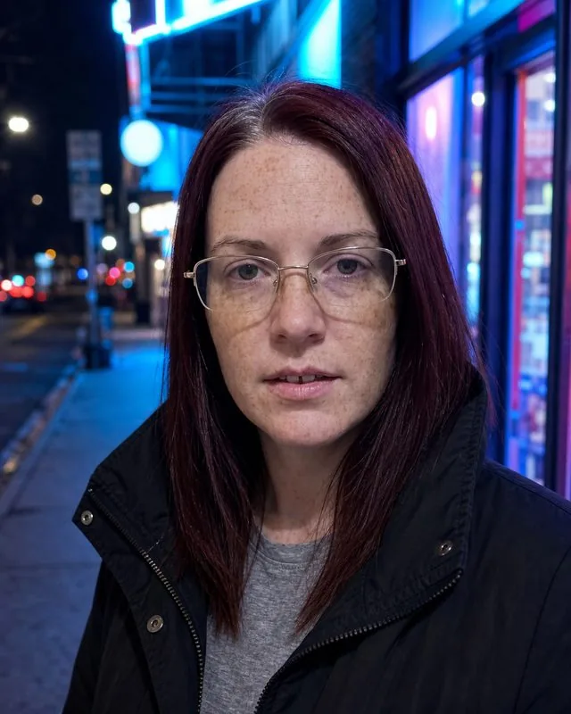 Night out: on a city pavement at night under neon shopfront signs, jacket collar up, cool colour cast