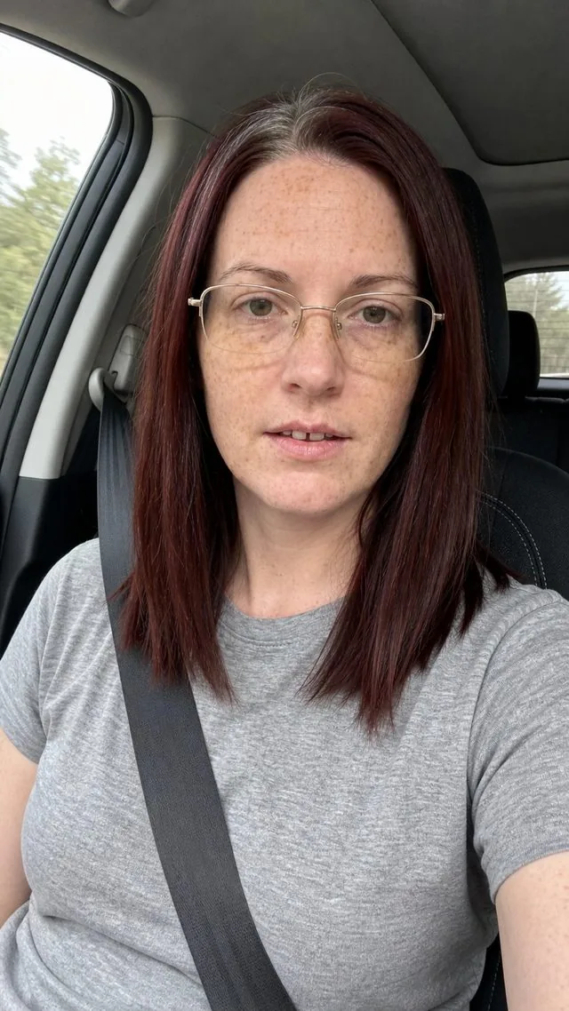 Front camera: a front camera selfie in a car passenger seat with seatbelt on, daylight through the window, casual expression