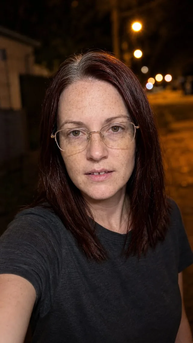 Front camera: a night-time front camera selfie with warm street lights bokeh behind, slight motion blur