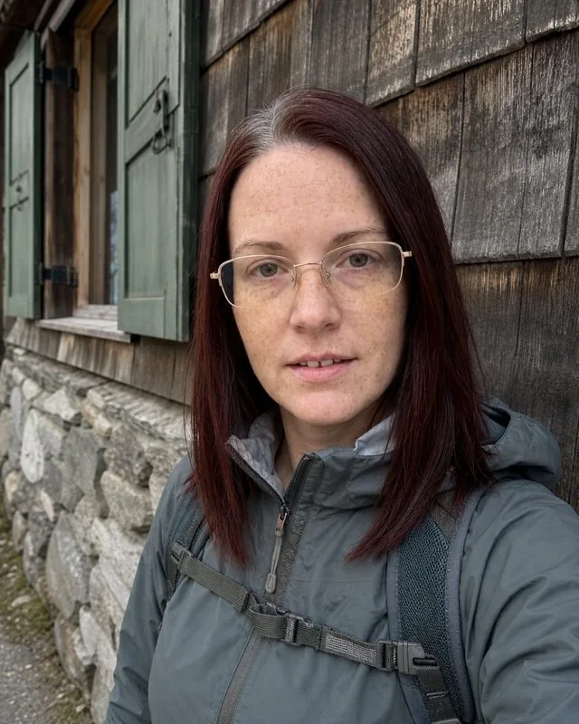 Gorpcore: against a mountain hut wall in a shell jacket with a small pack, flat overcast light