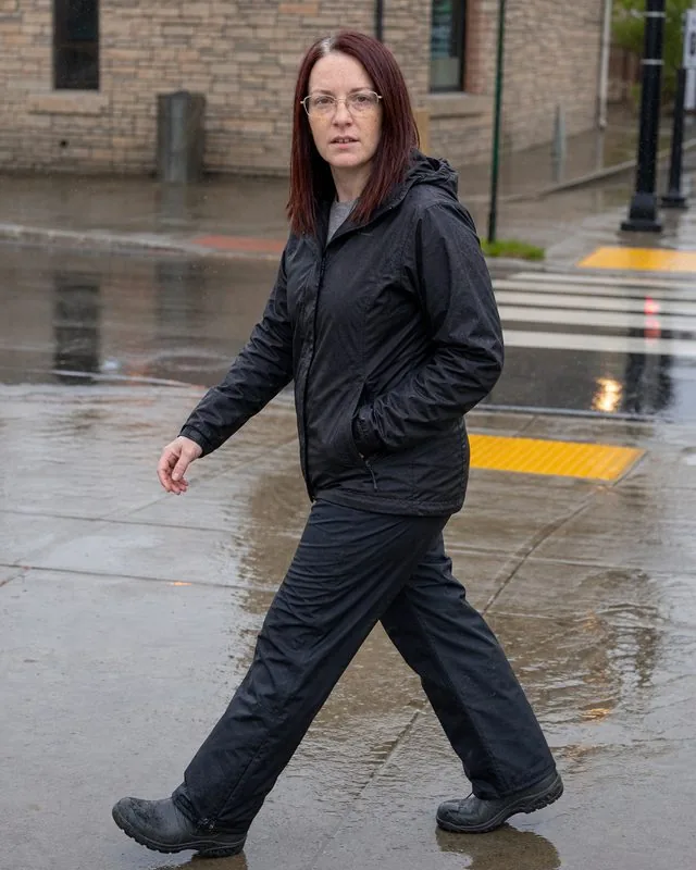Gorpcore: crossing a wet pavement in waterproof trousers and boots, reflections and drizzle in the air
