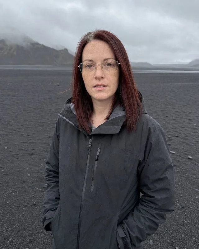 Iceland: standing on black volcanic sand in a heavy waterproof jacket, low grey cloud and distant mountains