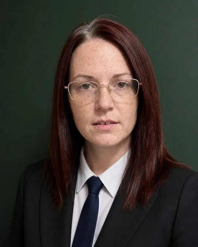 Lawyer: a tight headshot against a deep green wall, subtle key light, jacket and tie sharply pressed