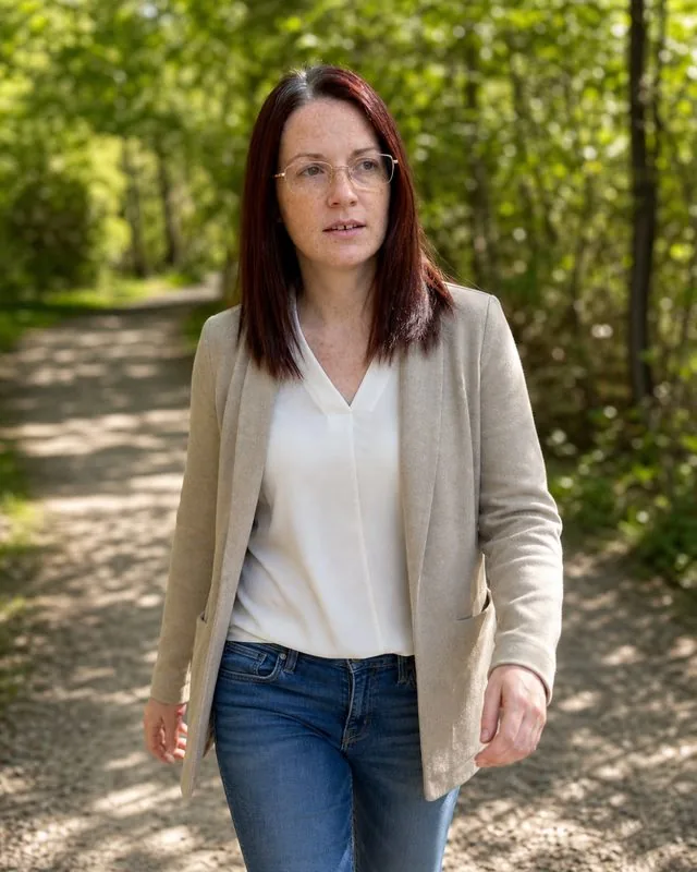 Life coach: walking outdoors on a sunny path in casual smart clothing, mid-stride, green blurred behind