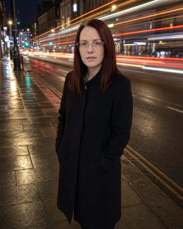 Long exposure: standing still on a night pavement while traffic light trails streak past, sharp figure against motion