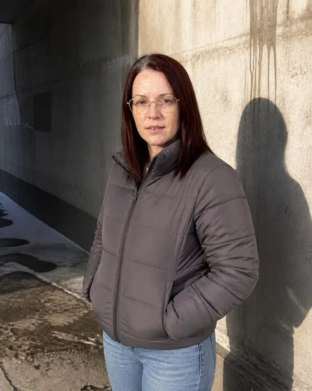 Puffer jacket: against a concrete underpass in a cropped puffer jacket, hands in pockets, hard shadow from a low winter sun