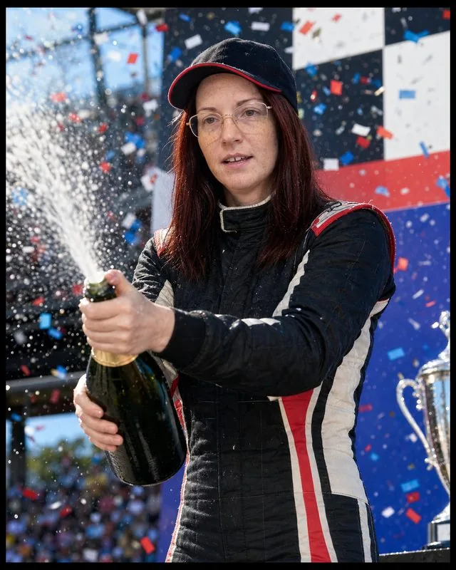 Race driver: on a podium spraying champagne in a racing suit and team cap, bright flashes and confetti in the air