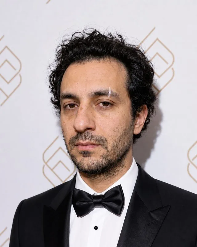 Red carpet: pausing for photographers with a step-and-repeat wall behind, black tuxedo, direct frontal flash