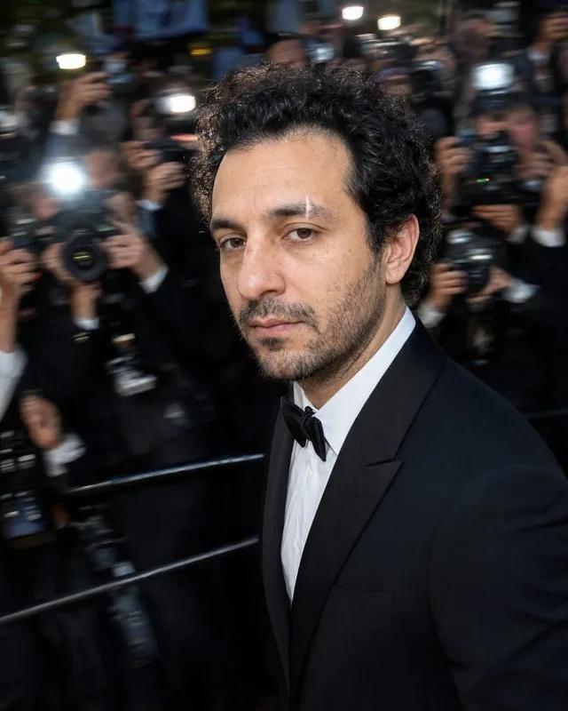 Red carpet: walking past a barrier of cameras in a tailored dinner jacket, motion blur around a sharply lit figure