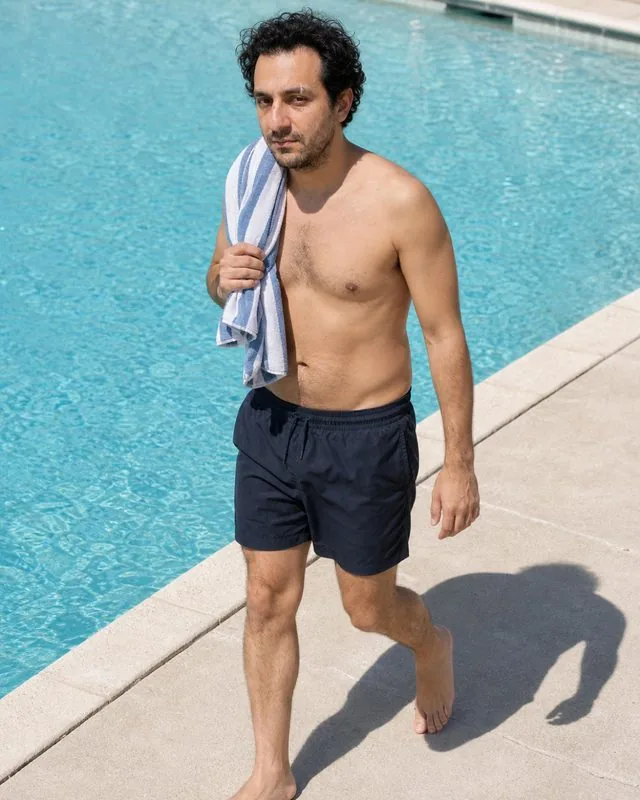 Resort: walking along a pool edge in swimwear with a towel over one shoulder, hard sun and sharp shadows