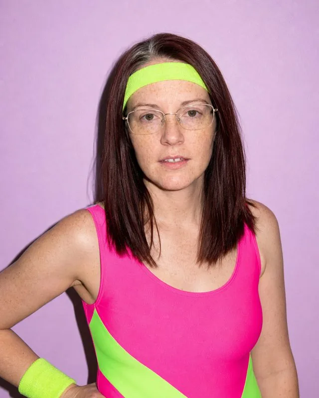 1980s: in neon aerobics clothing against a pastel wall, hard flash and high contrast