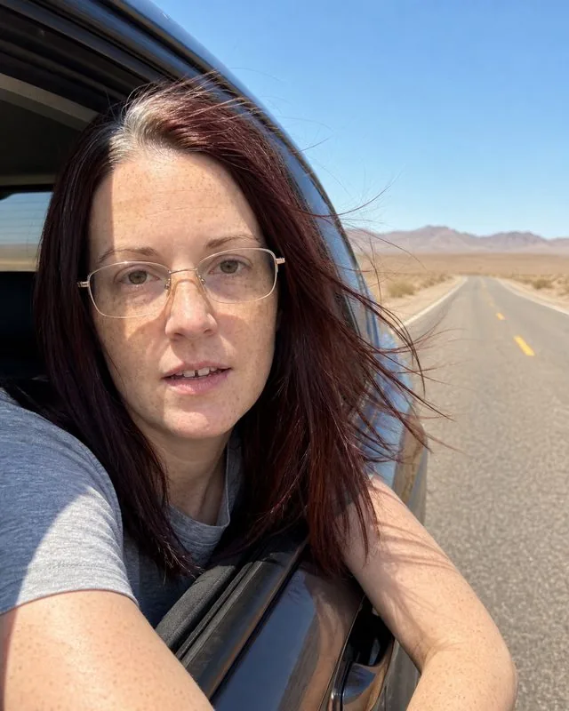 Road trip: leaning out of a car window on an empty desert road, wind in the hair, hard midday sun