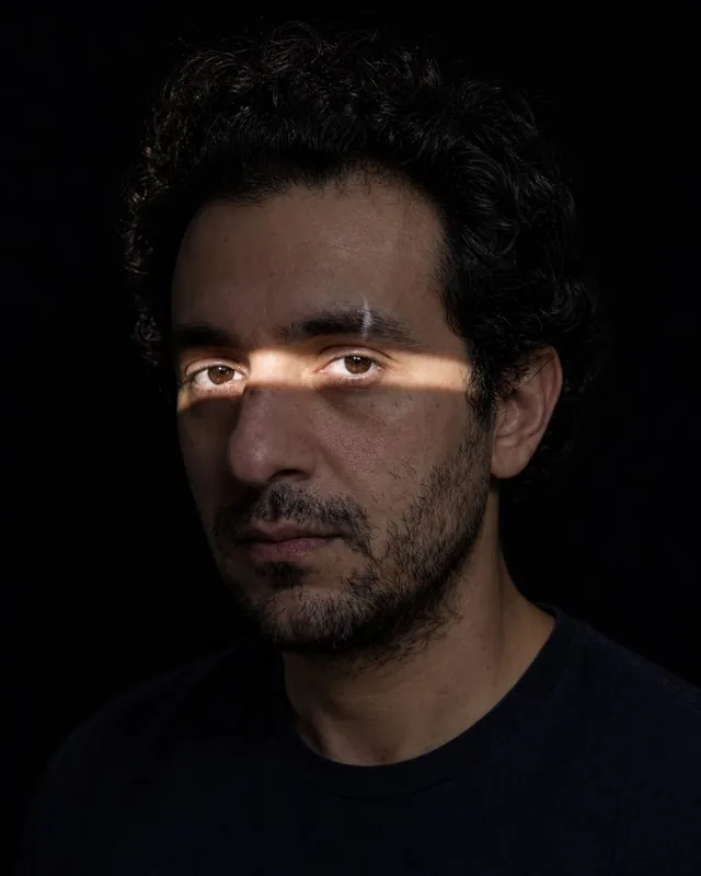 Smoke and shadow: half the face in deep shadow with a narrow slash of light across the eyes, black background