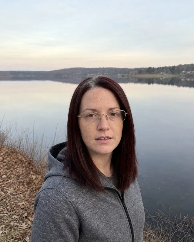 Spiritual: standing at the edge of a still lake at dawn, flat pale light and mirrored water