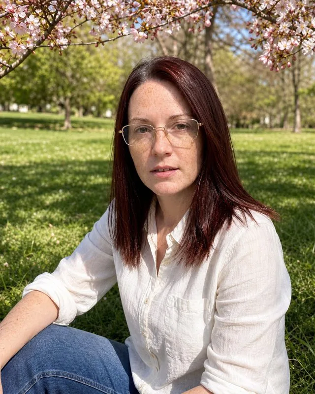 Spring blossom: sitting on grass in a park in a light cotton shirt, blossom branches framing the top of the frame