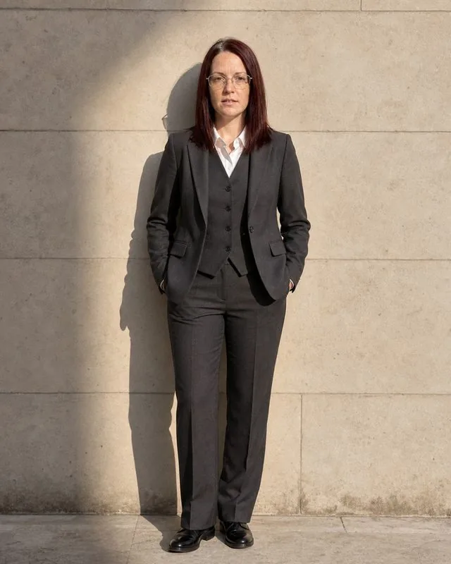 Tailored suit: a full-length frame in a sharply tailored three-piece suit against a plain stone wall, hard side light