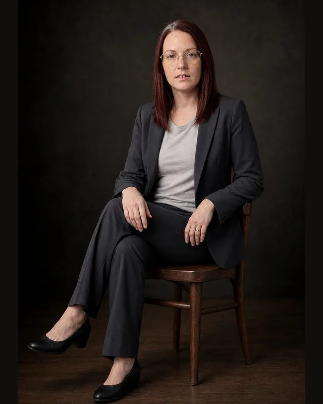 Tailored suit: seated on a wooden chair with legs crossed, jacket open, single soft key and deep background falloff