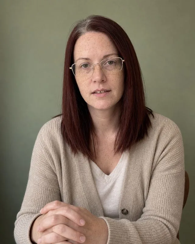 Therapist: a calm portrait against a muted sage wall, soft oatmeal cardigan over a plain top, soft diffused window light