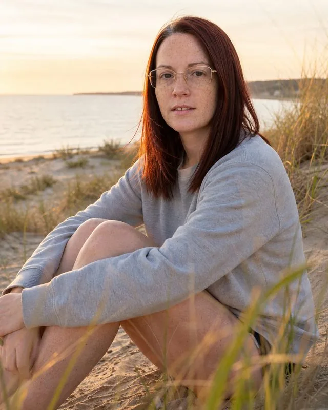 Beach sunset: sitting on a dune at last light with knees drawn up, cotton sweatshirt over swim shorts